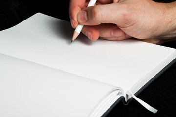 Male hand writing with a pencil in a blank book (close-up)