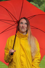 Eine Frau unter rotem Regenschirm verzieht das Gesicht wegen Regenwetter
