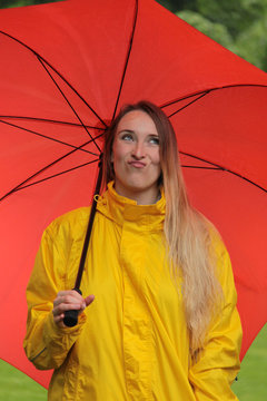 Frau unter rotem Regenschirm verzieht das Gesicht wegen Wetter