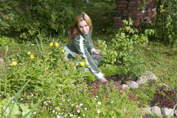Young pretty woman looks after behind plants in the garden