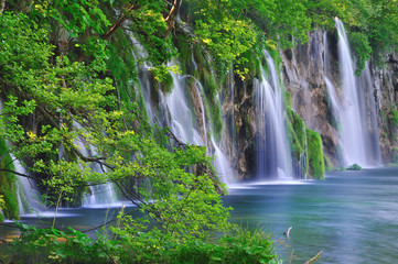 Wasserfälle, umgeben von Bäumen, fliessen in einen blauen See