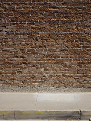 A textured red brick wall and sidewalk