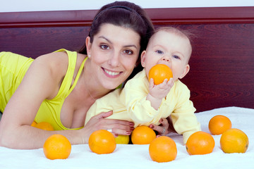 Mother and baby plays with oranges fruits
