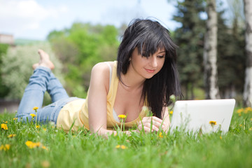 Naklejka na ściany i meble Cute woman with white laptop in the park with dandelions