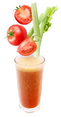 Slices of tomato and celery falling into a glass of fresh juice