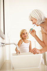 Grandmother Brushing Teeth In Bathroom With Granddaughter