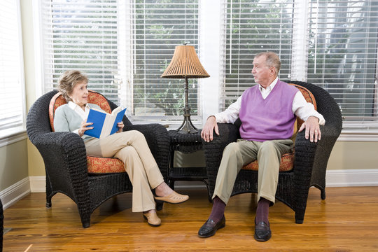 Senior couple sitting on living room chair reading