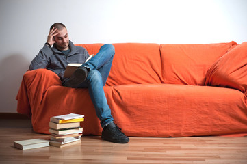 uomo seduto sul divano arancione che legge libro