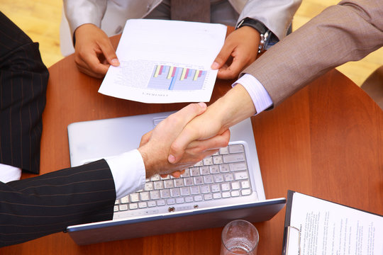 handshake over paper and pen,blurry computer in the background