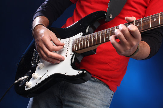 Detail of a musician playing a black electric guitar.
