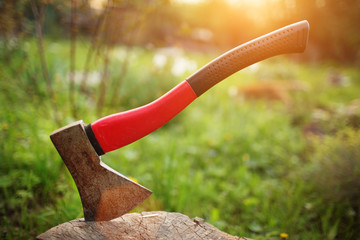 Red axe in stump on green lawn at sunset. Shallow DOF.