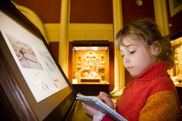 little girl standing near monitor writes to writing-books