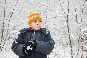 Fototapeta na wymiar boy keeps in hands snowball in wood in winter, looking aside
