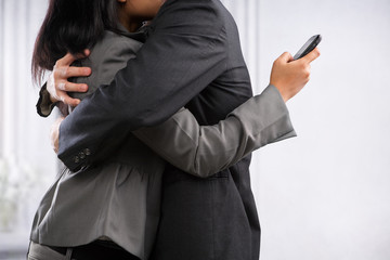 Business couple hug yet the woman still using cell phone