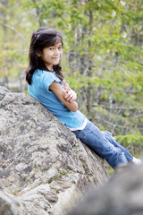 Little girl sitting against rock, smiling