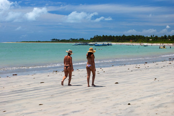 Girls walking on the green sea beach in Alagoas, Brazil
