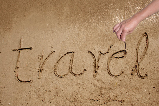Travel handwritten in sand on a beach