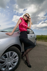 Blond girl in sunglasses is near a car on the road.