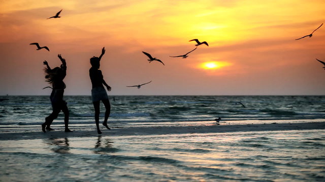 Girls on a beach at sunset with birds flying