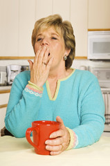 Yawning woman with red coffee mug in her kitchen