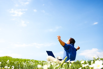 Man working with laptop in a meadow of flowers with copyspace