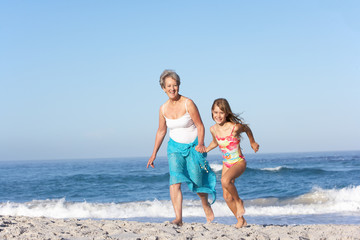 Grandmother Running With Granddaughter Along Sandy Beach