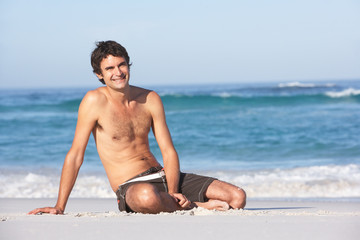 Fototapeta na wymiar Young ManWearing Swimwear Sitting On Sandy Beach
