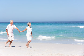 Fototapeta na wymiar Senior Couple On Holiday Running Along Sandy Beach