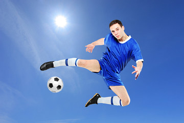 Soccer player with a ball in action against blue sky