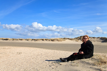 Fototapeta na wymiar Woman with dog sitting in the sand dunes on the beach