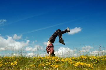 Young woman doing a cartwheel in a meadow - obrazy, fototapety, plakaty