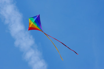 colorful kite flying below an aircraft vapor trail