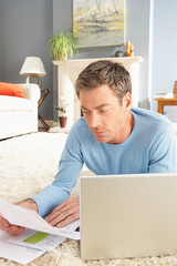 Man Using Laptop To Manage Household Bills Laying On Rug At Home