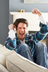 Excited Man Sitting On Sofa At Home Talking On Phone