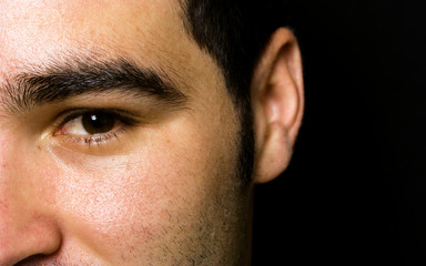 Obraz premium half of the face portrait of an young man on black background