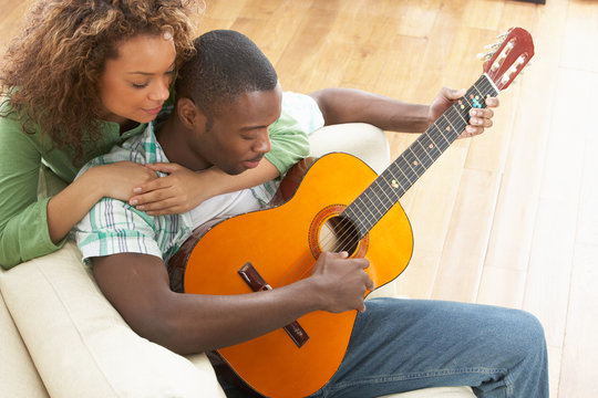 Young Couple Relaxing Sitting On Sofa Playing Acoustic Guitar