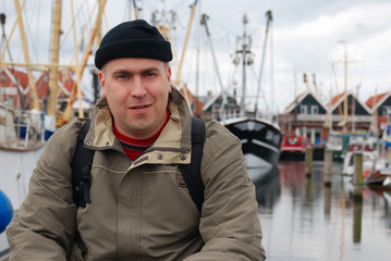 Obraz premium Man sitting at the Urk town pier with the boats at background.