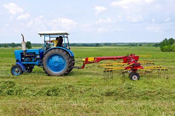 A tractor turning cut hay in a field.