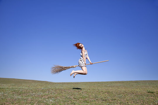 Young witch with broom at field