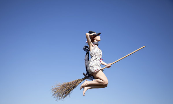 Young witch with broom flying in sky