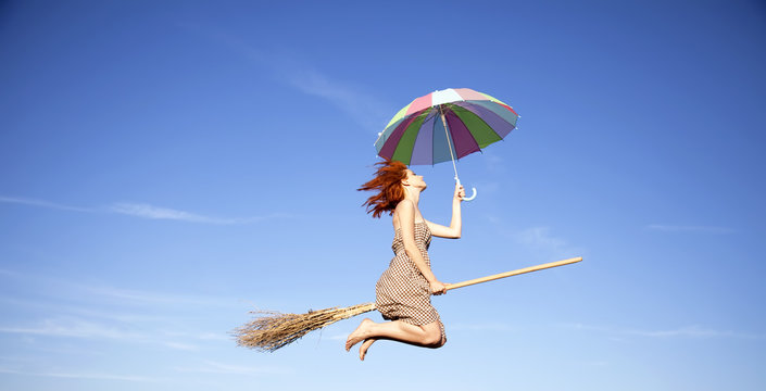 Young witch with broom and umbrella flying in sky