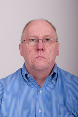 Obraz premium Older Balding Man in Blue Shirt Holding Chin Up Looking Through