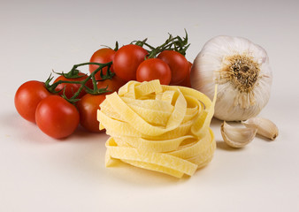 raw taglatelle tomatoes and garlic on white background