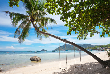 Tropical beach with swing and palms under blue sky. Thailand