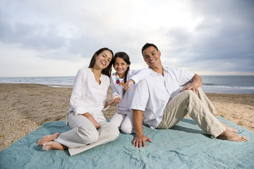 Fototapeta premium Hispanic family sitting on blanket at beach