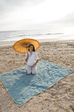 Hispanic Woman With Parasol On Beach Blanket