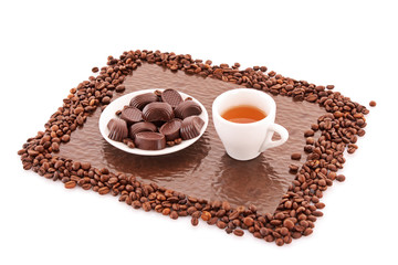 Assorted chocolate candies and cup of tea on brown background