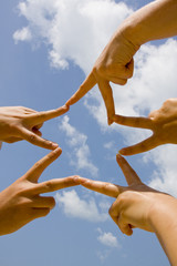 Many hands connecting to star shape under sky