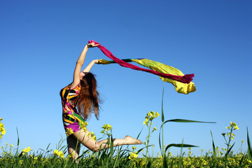 Pretty girl in the summer  jumping on the field with a scarf