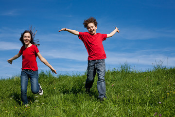 Girl and boy jumping, running against blue sky